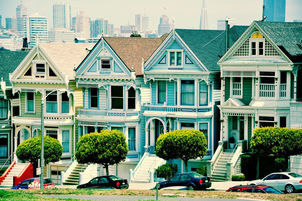 Brightly painted Victorian houses on a San Francisco street with the downtown skyline behind them