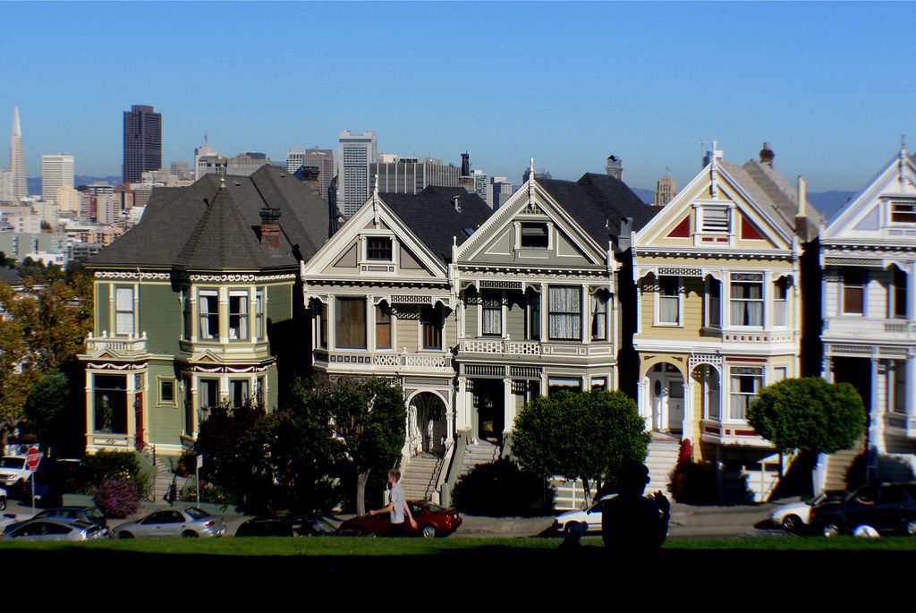 A row of Victorian houses in San Francisco with the downtown skyline rising behind them